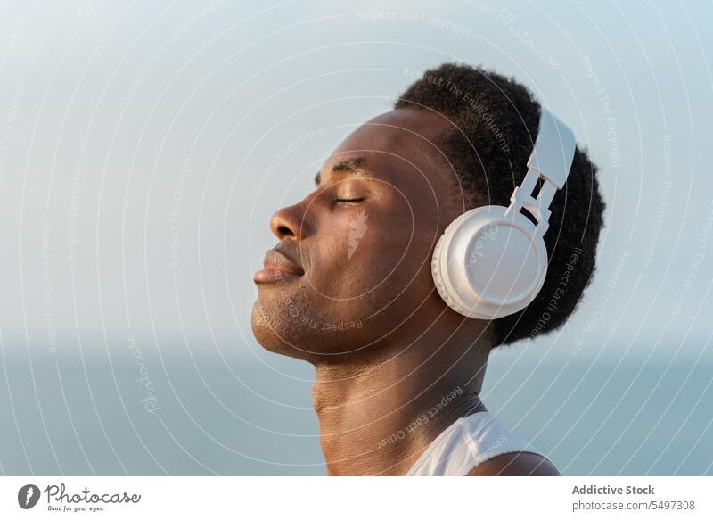 Nachdenklicher schwarzer Mann mit Kopfhörern am Meer Musik zuhören besinnlich MEER Gesang Drahtlos Porträt Klang Gerät männlich Wasser Melodie Windstille ruhig