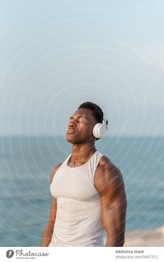 Nachdenklicher schwarzer Mann mit Kopfhörern am Meer Musik zuhören besinnlich MEER Gesang Drahtlos Klang Gerät männlich Wasser Melodie Windstille ruhig