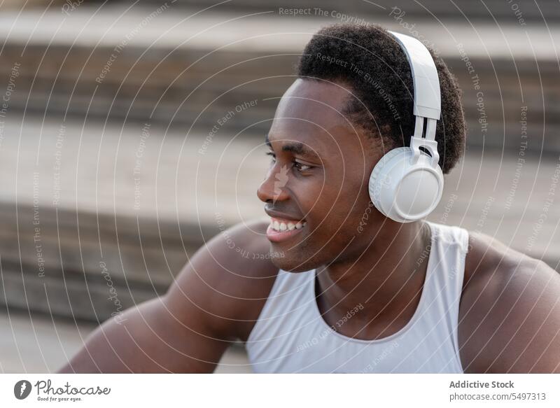 Begeisterter schwarzer Sportler mit Kopfhörern, der Musik genießt Athlet zuhören Gesang Treppenhaus Porträt männlich Afroamerikaner Model passen muskulös stark