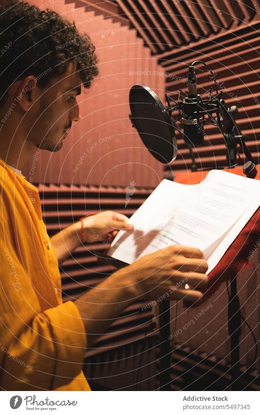Nachdenklicher junger ethnischer Mann sitzt und liest Papiere auf einem Schreibtisch in einem Studio lesen Mikrofon ernst Hand am Kinn nachdenklich besinnlich