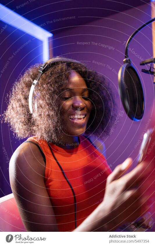 Schwarze Frau singt und kreiert ein Lied Sängerin singen Aufzeichnen kreieren hohe Note Mikrofon Kopfhörer Musik Atelier schwarz Afroamerikaner Smartphone