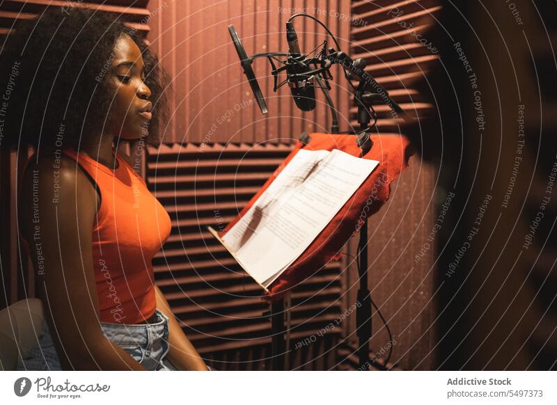 Fokussierte schwarze Frau, die in der Nähe von Mikrofonen im Studio steht und ein Lied aufnimmt Sänger Atelier Aufzeichnen Gesang Papier Audio singen jung