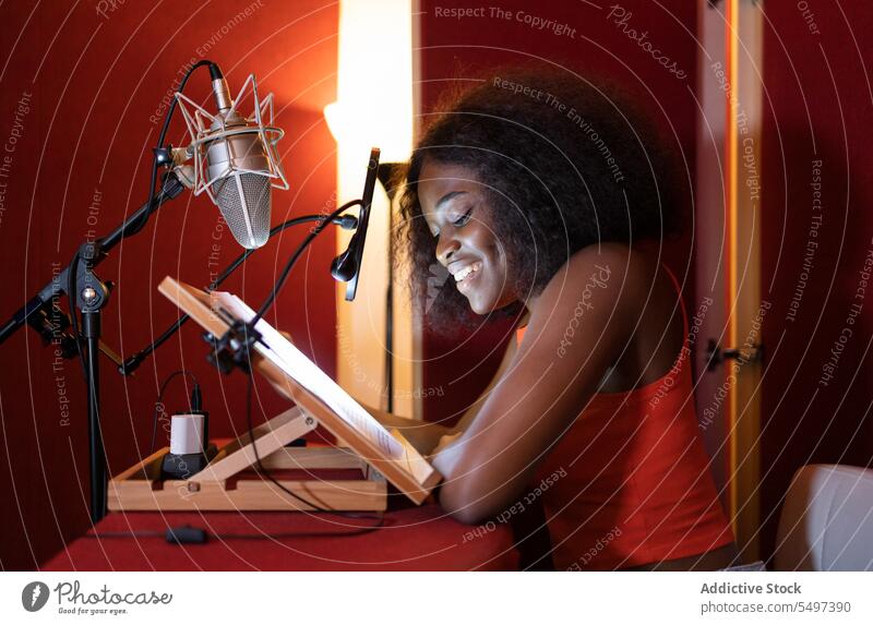 Lächelnde junge schwarze Frau, die am Schreibtisch sitzt und einen Podcast aufnimmt Wirt Ausstrahlung Aufzeichnen Mikrofon Radio Gerät Atelier Afroamerikaner