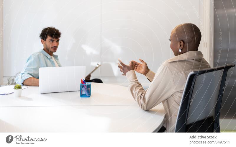 Verschiedene Kollegen besprechen ein Projekt im Büro, während sie mit einem Laptop am Tisch sitzen Mann Frau diskutieren professionell Gespräch männlich jung