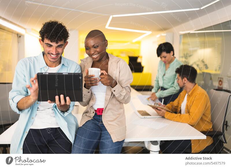 Verschiedene glückliche Kollegen nutzen gemeinsam ein Tablet Zusammensein benutzend Tablette Büro Arbeit Laptop Lächeln Apparatur vielfältig heiter Browsen