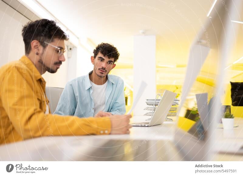 Männliche Kollegen arbeiten in einem modernen Büro zusammen Männer Papier Laptop benutzend Projekt Arbeit Mitarbeiterin Arbeitsplatz männlich Job Business