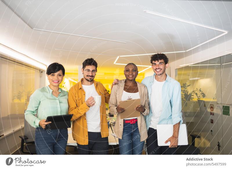 Glückliche multiethnische Mitarbeiter, die zusammen im Büro stehen Kollege Zusammensein Laptop Mitarbeiterin Arbeitsbereich Arbeitsplatz Tablette Lächeln Mappe