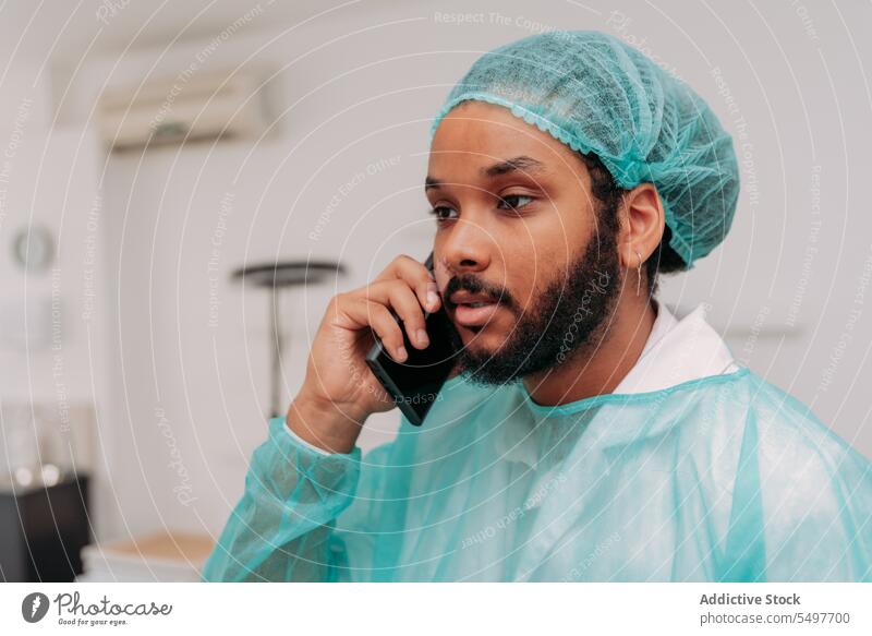 Ethnischer männlicher Arzt beim Telefonieren in der Klinik Mann Smartphone reden Chirurg ernst Telefonanruf Krankenhaus Konzentration Arbeit Chirurgie