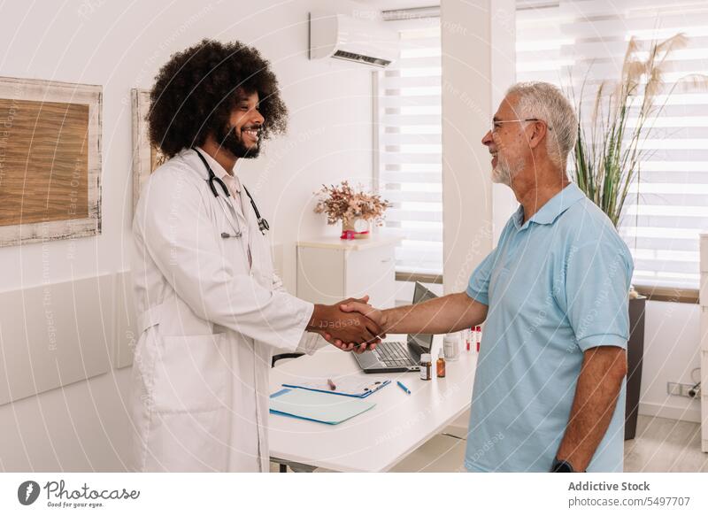 Fröhlicher, vielseitiger Arzt und Patient beim Händeschütteln Männer geduldig Hände schütteln Krankenhaus medizinisch heiter Lächeln Glück Klinik männlich
