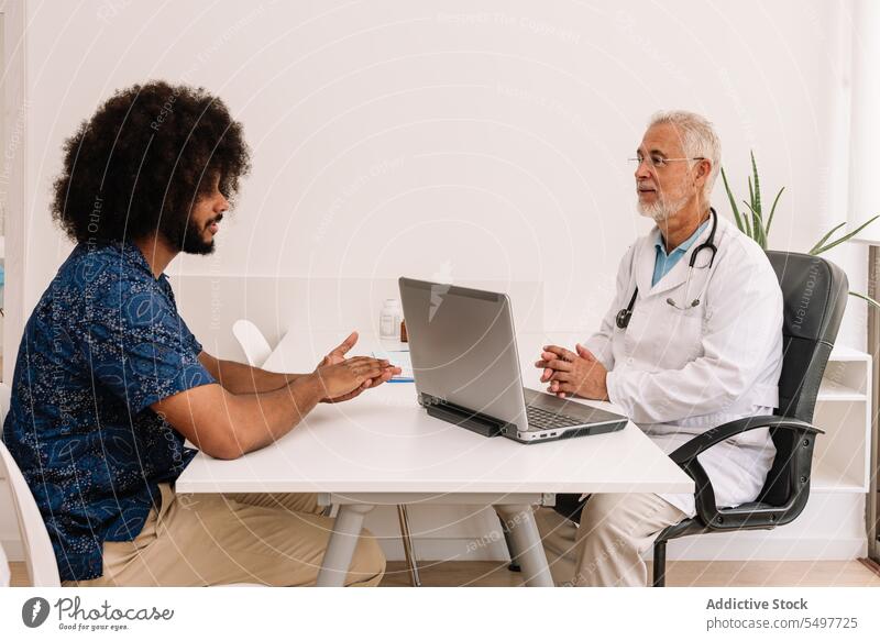 Älterer Mann diagnostiziert einen schwarzen Patienten bei einem Termin Praktiker geduldig Sanitäter Klinik prüfen konsultieren diagnostizieren Ernennung Laptop