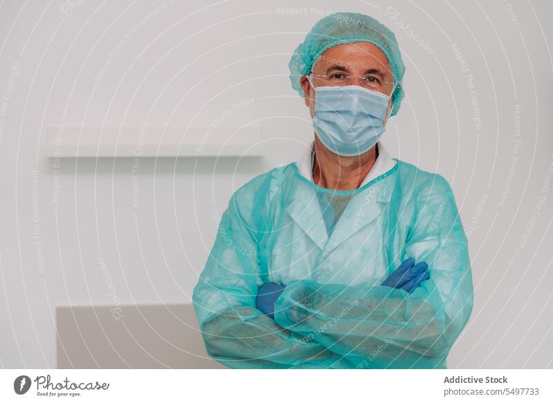 Zufriedener männlicher Chirurg mit verschränkten Armen in der Klinik stehend Mann Arzt die Arme verschränkt Glück Sanitäter Gesundheitswesen Porträt Krankenhaus