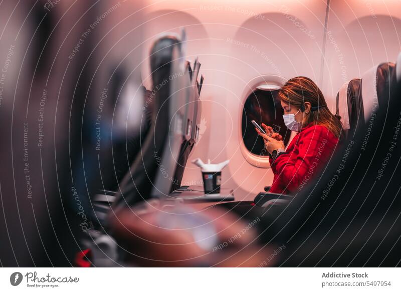 Frau trägt Maske und benutzt Smartphone im Flugzeug Passagier benutzend Mundschutz Coronavirus Sitz Sicherheit behüten Nacht neue Normale Bund 19 Mobile