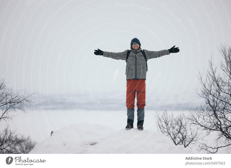 Fröhlicher Mann mit ausgestreckten Armen auf verschneitem Terrain stehend Schnee Winter Wald Natur ausdehnen Oberbekleidung Glück Finnland warme Kleidung kalt