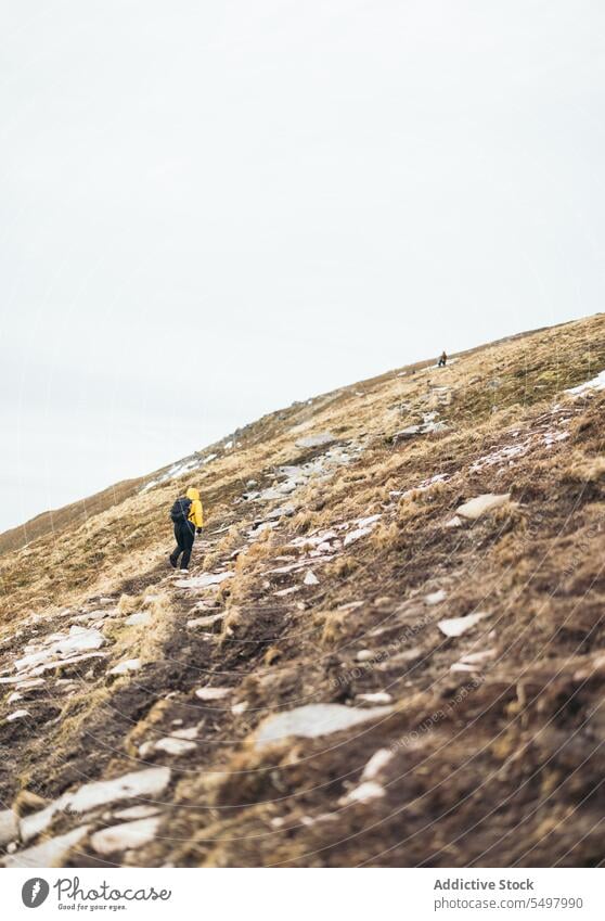 Unbekannter Wanderer mit Rucksack, der bei Tageslicht einen felsigen Trockenrasenhügel erklimmt Reisender Trekking Landschaft Hügel Natur Aufstieg Sommer