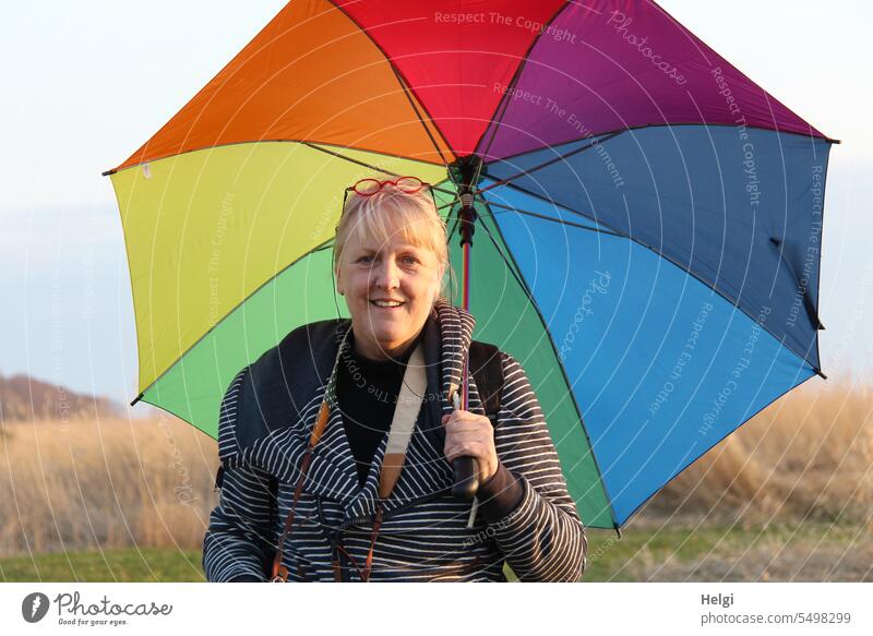 Porträt einer freundlichen blonden Frau mittleren Alters, die einen bunten Regenschirm hält Mensch Freundlichkeit Lächeln sympathisch Erwachsene feminin