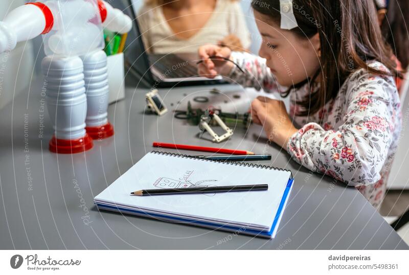 Roboter, der von einem Kind auf einem Notebook gezeichnet wurde, und Student, der im Hintergrund ein Kabel in einem Stromkreis anschließt Kinder zeichnen
