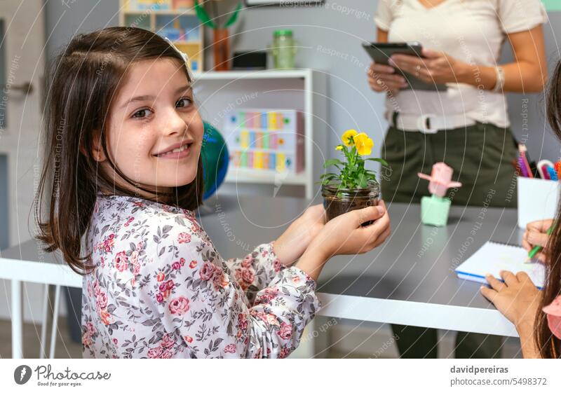 Studentin schaut in die Kamera, während sie eine Stiefmütterchenpflanze im Ökologie-Klassenzimmer hält Schüler Frau Beteiligung Pflanze Blume Klassenraum Blick