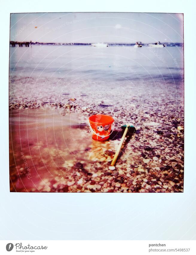 ein sandeimer und eine schaufel im wasser am seeufer. kinderspielzeug polaroid Ferien & Urlaub & Reisen See Gardasee Seeufer urlaubsfoto italien Außenaufnahme