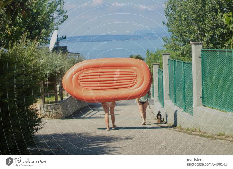 zwei frauen in bikini tragen ein oranges schlauchboot in see gardasee nackte haut retro hund hundeleine badegäste Sommer Farbfoto urlaub italien