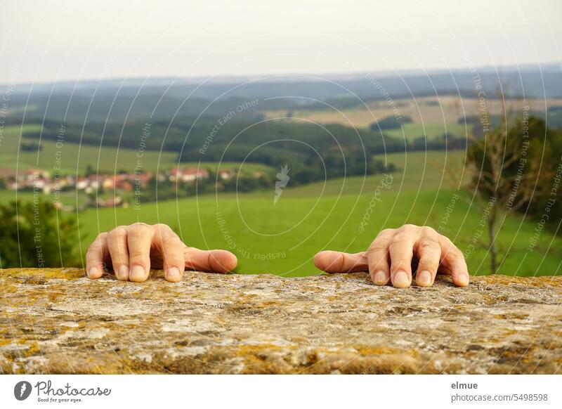 zwei Hände klammern sich an altes Mauerwerk vor bewaldetem Hügelland festhalten klettern Notfall Anstrengung Weitblick Gefahrensituation Spaß Blog Risiko Stein