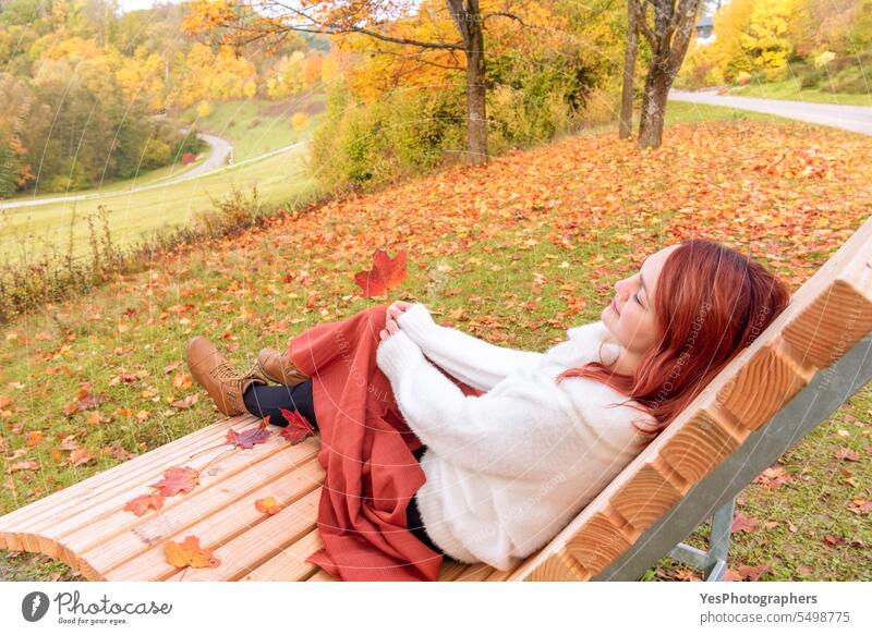 Frau sitzt auf einer Bank in einer Herbstlandschaft. im Freien allein schön Schönheit Decke Stiefel hell lässig Farbe farbenfroh genießen fallen Laubwerk