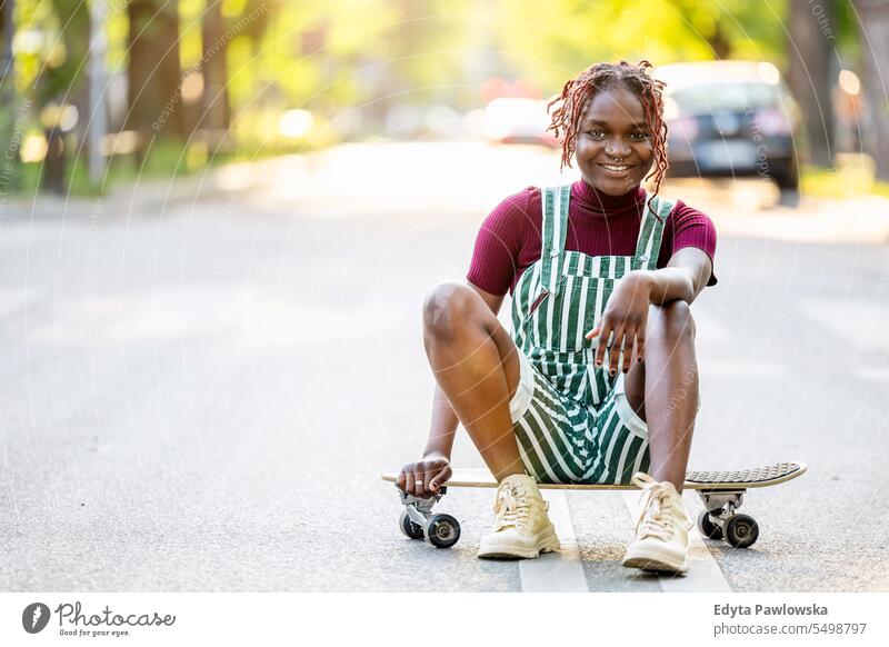 Porträt einer schwarzen nicht-binären Person mit einem Skateboard auf der Straße sitzend echte Menschen positiv selbstbewusst Erwachsener junger Erwachsener