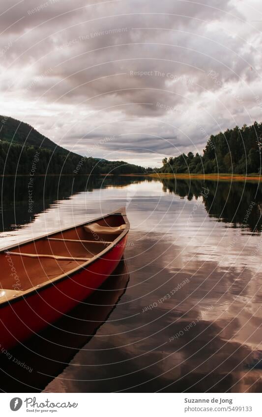 Hölzernes Kanu auf einem Fluss in Schweden. Die Wolken spiegeln sich im Fluss. Das Bild hat eine malerische, ruhige und friedliche Ausstrahlung. Das Wetter ist bewölkt, aber die Stimmung ist fröhlich.