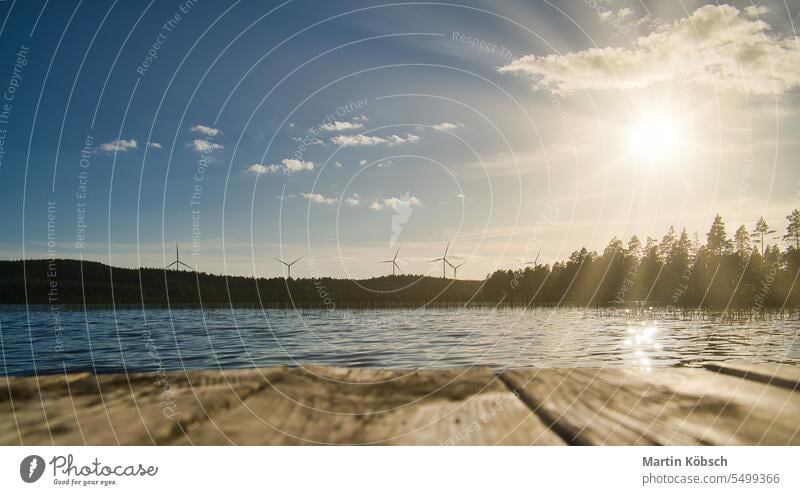 Blick über einen Steg auf das blaue Wasser eines Sees. Windräder im Hintergrund. Baden Abend schön Windturbinen Elektrizität Erneuerbare Energie Abenddämmerung