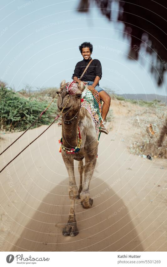 ein junger Mann sitzt auf den Rücken eines Kamel und reitet durch die Wüste Junger Mann männlich gutaussehend im Freien Menschen Sahara Porträt draußen Tourist
