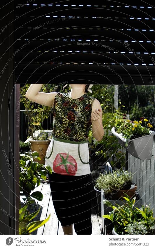 Frau steht auf dem Balkon und trinkt etwas, ihr Gesicht ist vom Rolladen der Balkontür verdeckt Terrasse begrünt Pflanzen Garten Topfpflanzen Gartenarbeit Natur