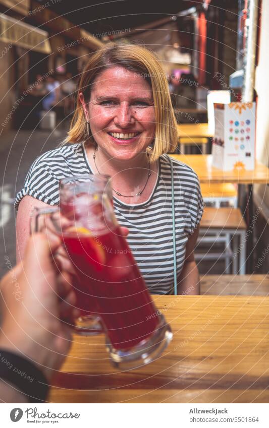 junge Frau mit blonden mittellangen Haaren sitzt an einem Tisch und stößt mit einem Glas mit Tinto de Verano an Granada Rotwein Spanien Andalusien Bar Tapasbar