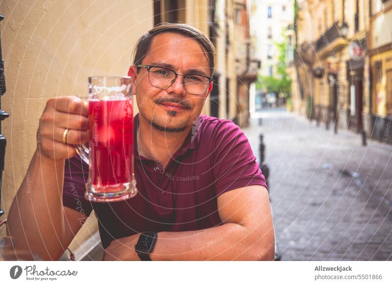 junger Mann mit Brille und kurzen Haaren sitzt an einem Tisch und hält ein Glas mit Tinto de Verano Granada Rotwein Spanien Andalusien Bar Tapasbar Erfrischung
