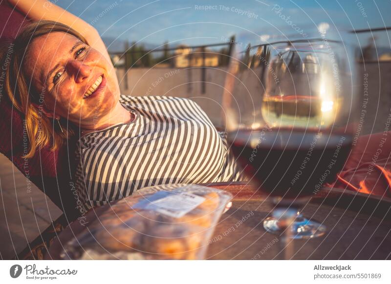 junge hübsche blonde Frau lässt im Sonnenuntergang den Tag mit einem Glas Weißwein auf der Terrasse ausklingen Spanien Andalusien Granada Sommer Hitze Schatten