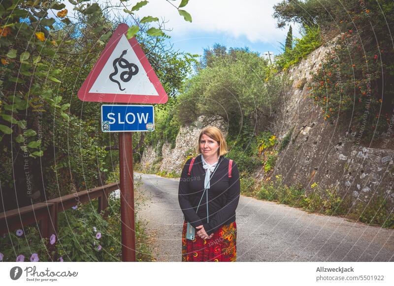 blonde Frau mittleren Alters schaut ängstlich neben einem Schild dass vor Schlangen warnt Schilder & Markierungen Warnschild Schlangenwarnung Angst