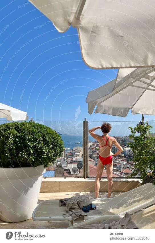 Frau schaut auf Istanbul Badeanzug Aussicht rot Bosporus Sonnenschirme Liegestühle Hotel Buchsbaum Glasscheibe Sommer blauer Himmel Urlaub Erholung