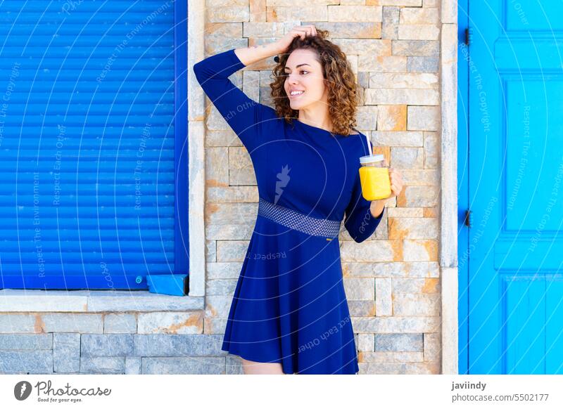 Lächelnde Frau mit Saft auf einer Stadtstraße Getränk Tastkopf Straße trinken Glas Sommer Gebäude schäbig Großstadt positiv jung Glück krause Haare heiter Stil