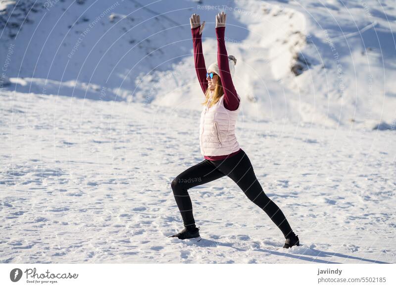 Schlanke Frau streckt sich in Kriegerpose über verschneiten Bergen Yoga Winter üben Schnee Dehnung Gleichgewicht Pose Wellness Natur Harmonie virabhadrasana