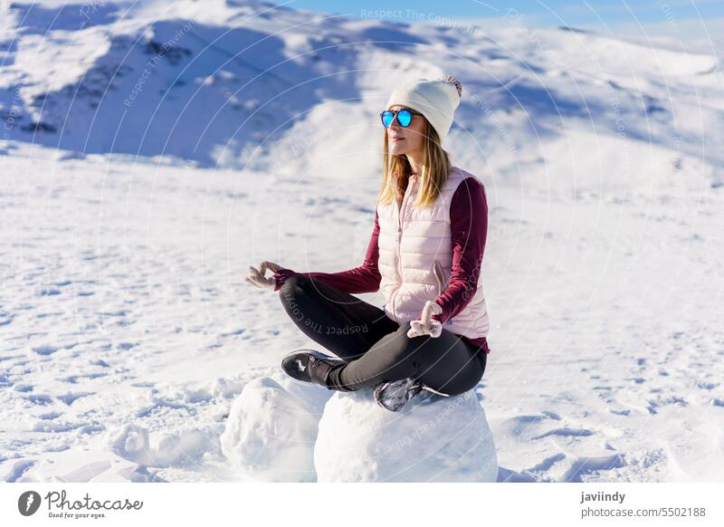 Fröhliche Frau meditiert im Lotussitz auf Schnee Lotus-Pose meditieren Natur Winter sich[Akk] entspannen Tourismus padmasana ruhen Sonnenbrille Urlaub jung
