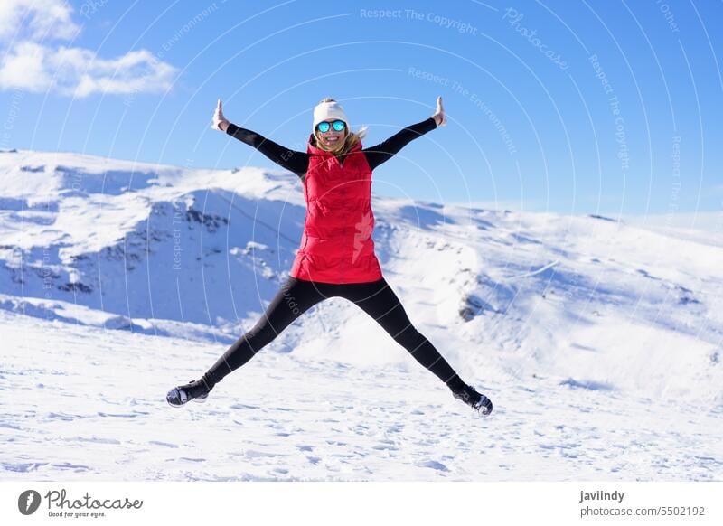 Fröhliche Frau in warmer Kleidung, die auf einem Schneegelände in die Luft springt aufgeregt springen Glück Berge u. Gebirge Winter aktiv Energie genießen jung