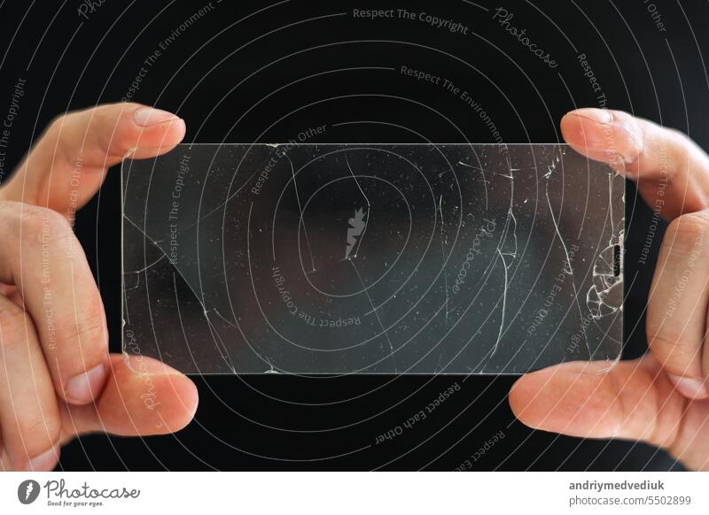 Zerbrochenes Schutzglas für den Touchscreen eines Smartphones in den Händen eines Telefonmechanikers auf schwarzem Hintergrund. Dienstleistungen zum Kleben und Ersetzen von beschädigtem Schutzglas. Reparatur-Konzept