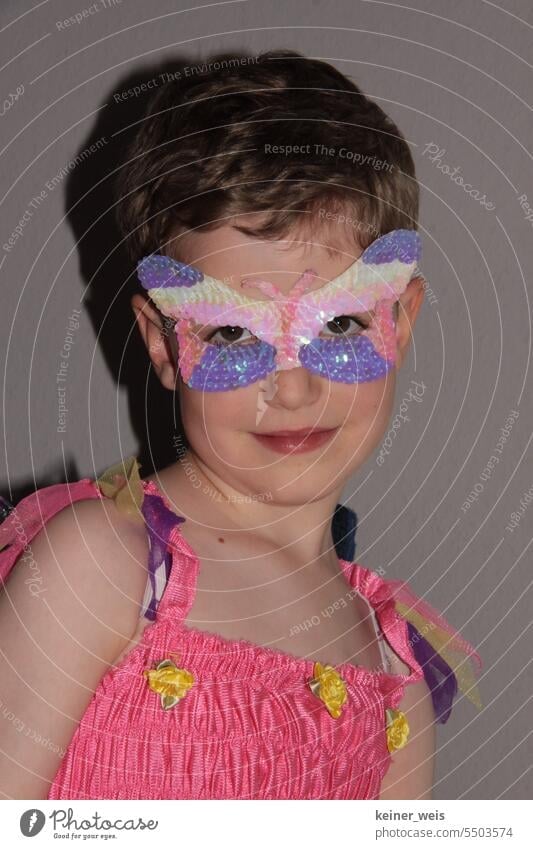 Ein Kind im Kleid und einer Schmetterlingsmaske im Gesicht über den Augen Kostüm Lächeln Maske Fee männlich weiblich unisex egal gender Karneval Karnevalskostüm