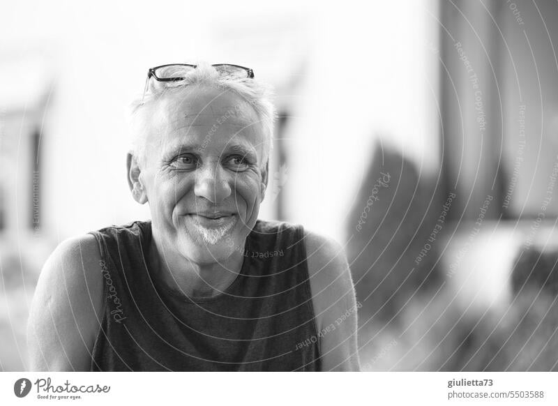 Drinkje bej Inkje | Schwarz-weiß-Porträt, Mann mit Kinnbart und Brille auf dem Kopf, freundlich, lächelnd, glücklich Schwarzweißfoto Mann mittleren Alters