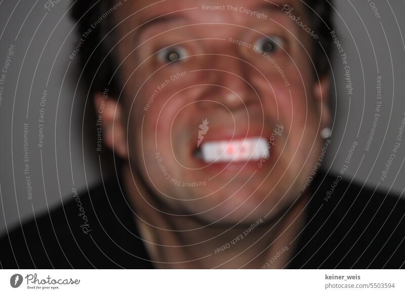 Ein Mann zeigt gruselig leuchtende weiße und rote Zähne in einer unscharfen Fotografie mit Zahnbeleuchtung Gruselig Gesicht Abbildung Horror Cheapness Mensch