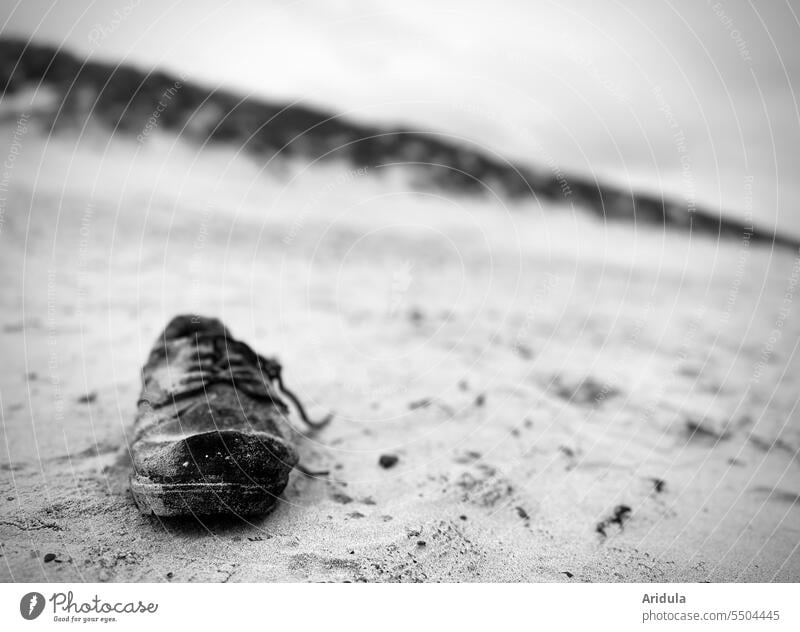 Alter schwarzer Schnürschuh am Strand mit Düne im Hintergrund s/w Schuh Schnürsenkel Sand Strandgut alt verloren Schwache Tiefenschärfe Natur Einsamkeit