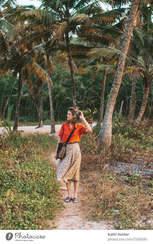 eine junge Frau in einer roten Bluse steht am Strand mit vielen Palmen im Hintergrund Kokospalme Sommer Kokosnuss Baum exotisch Landschaft Pflanze
