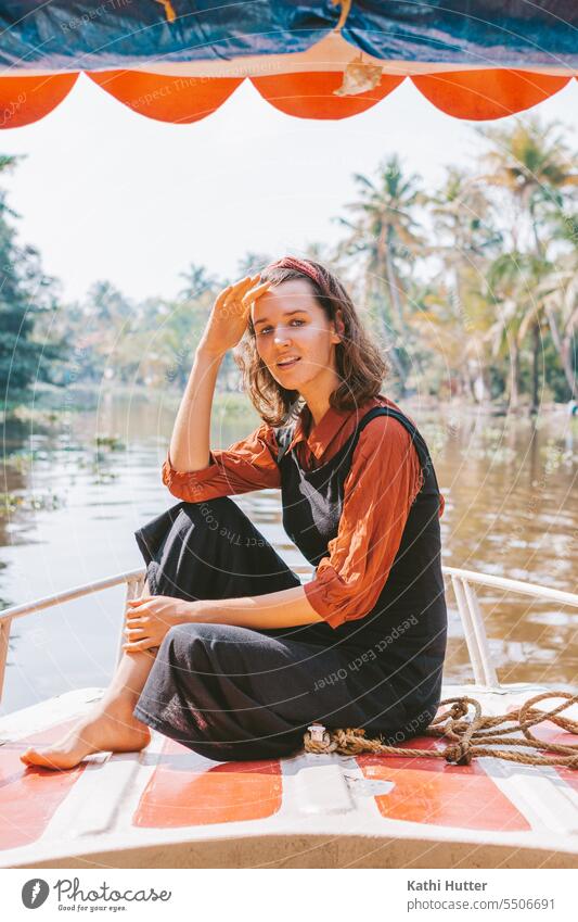 eine junge Frau in einem schwarzen Kleid, sitzt auf einem Boot in the Backwaters von Kerala. hübsch attraktiv natürlich Schönheit Person Mädchen Lifestyle