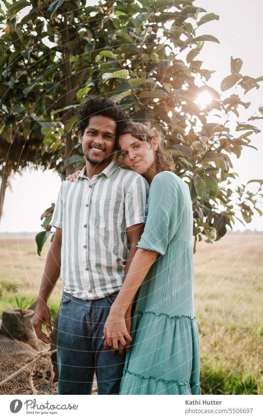 eine junge Frau und ein junger Mann halten Händchen vor einem Baum durch welchen die Sonnenstrahlen scheinen romantisch Paar Liebe Zusammensein Glück Romantik