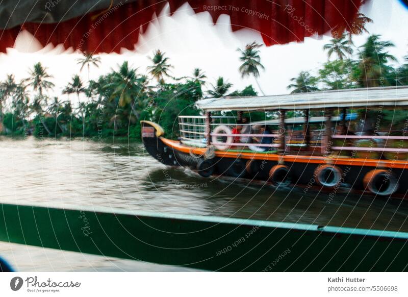 ein Boot fährt in den Backwaters von Kerala an einem anderen Schiff vorbei. Im Hintergrund sieht man viele Palmen. Schifffahrt Außenaufnahme Hafen Wasser Tau