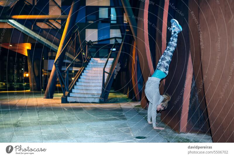 Frau macht Handstand-Übung gegen eine Blechwand in der Stadt bei Nacht jung Tun Sport Körperhaltung positionieren Flexibilität Pilates Yoga stehen Pose Training
