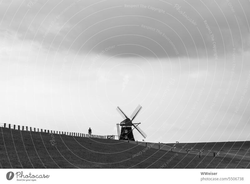 In der Ferne läuft eine Person über den Deich auf eine Windmühle zu minimalistisch allein miniatur Mühle traditionell historisch original Damm Nordsee Himmel
